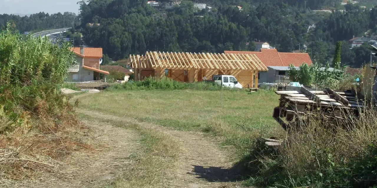 Terreno rural con construcción de madera, casas y vegetación. Se observa un camino de tierra y una posible servidumbre de acueducto en el paisaje.