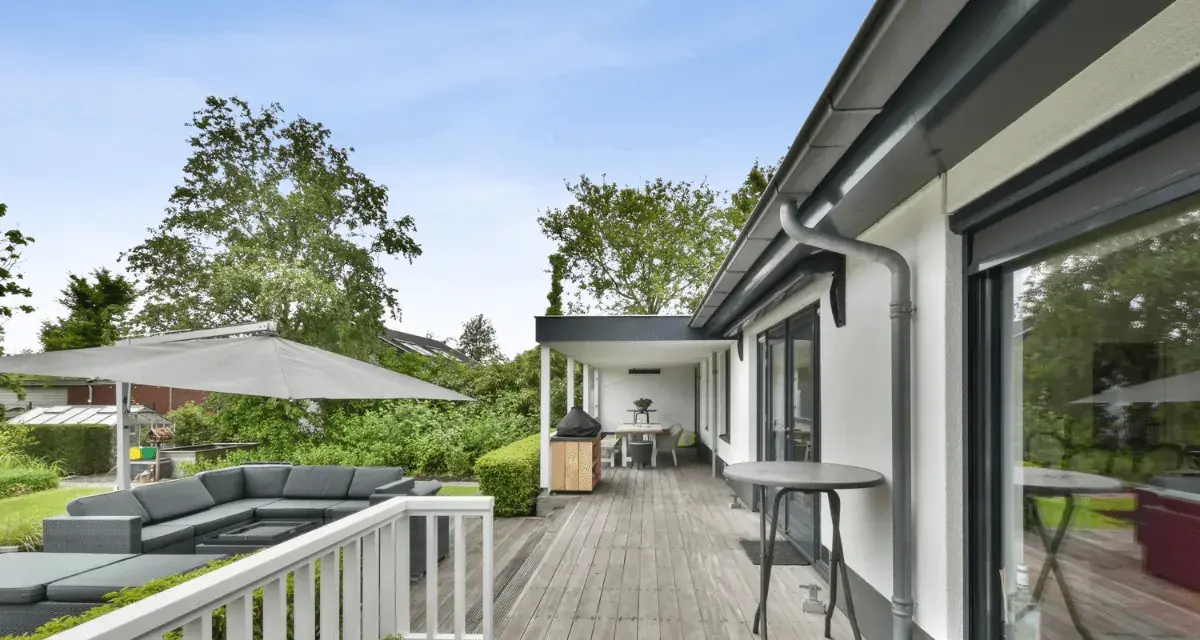 Un porche moderno con muebles de exterior, sombrilla y barbacoa. Ideas para como cerrar un porche y disfrutarlo todo el año.