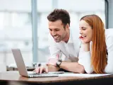 Pareja joven sonríe mientras busca en laptop. Podría ser sobre ayuda compra vivienda jovenes.