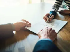Manos firmando un contrato de alquiler de piso. Los padres avalan el alquiler.