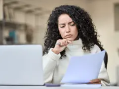 Mujer pensativa revisa documentos, preguntándose si un vecino puede cobrar por llevar la comunidad.