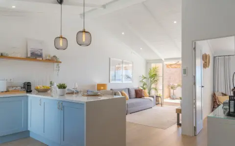 Cocina y sala de estar luminosas, perfectas para decorar casa playa poco presupuesto. Muebles claros, plantas y detalles náuticos crean un ambiente fresco.