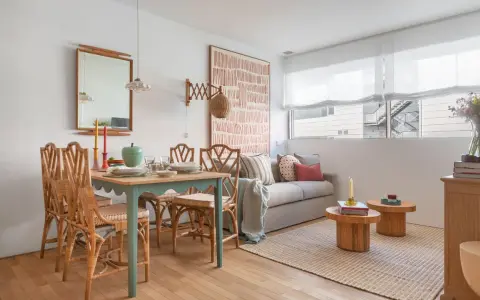 Ideas para decorar un piso pequeño con poco dinero: mesa de comedor de ratán, sofá acogedor y arte de pared llamativo.