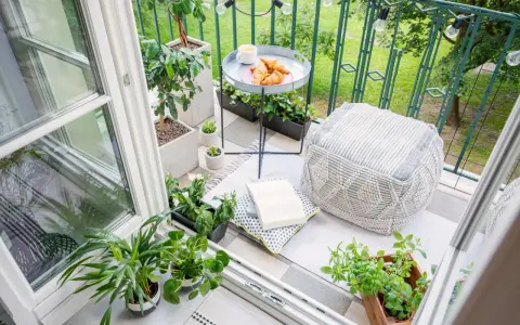 Acogedor rincón en unas terrazas cerradas pequeñas, con plantas, cojines, un libro y un café con cruasanes.