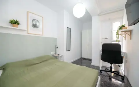 Habitación luminosa con cama, escritorio y armario. Ideal como piso para estudiantes, con decoración moderna y plantas.