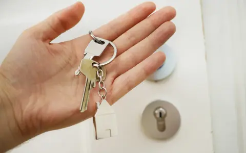 Mano sosteniendo llaves con un llavero de casa. ¡Por fin llega el día cuando pagan la ayuda del alquiler y se puede empezar a soñar con un nuevo hogar!