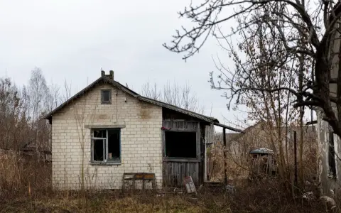 Casa de ladrillo blanco, abandonada, con ventanas rotas y vegetación seca. Un ejemplo de la ley sobre casas abandonadas.