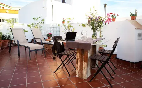 Terraza con tumbonas, mesa y sillas, ideal para uso privativo. Flores y plantas decoran el espacio.
