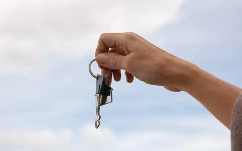 Mano sostiene un llavero con dos llaves y un dije de casa. La custodia llaves comunidad representa el acceso a un hogar compartido.
