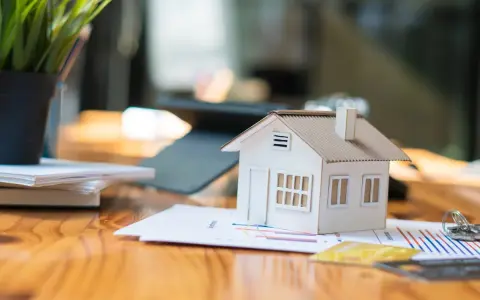 Maqueta de casa sobre gráficos, sugiriendo cómo saber si una casa tiene cargas. Llaves y tarjetas de crédito cerca.