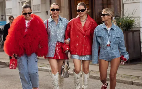 Cuatro mujeres pasean con atuendos llamativos. Una lleva un abrigo rojo voluminoso, otra un conjunto de lentejuelas azules y falda roja. Los colores que pegan con el rojo son el azul y el plateado.