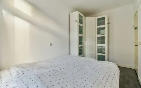 Un armario blanco con puertas de cristal es una solución ideal para saber donde colocar el armario en un dormitorio pequeño, maximizando el espacio.