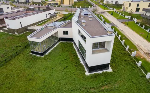 Casa moderna con grandes ventanales y tejado plano, rodeada de césped. Se puede poner una casa prefabricada en un terreno urbano como esta.