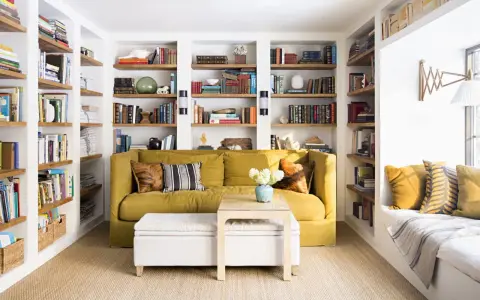 Sofá amarillo y estanterías llenas de libros, como si fueran casas que no necesitan permiso de obra. Un espacio acogedor para leer.