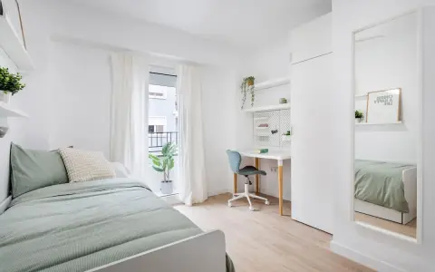 Habitación de estudiante con cama, escritorio, silla y espejo.