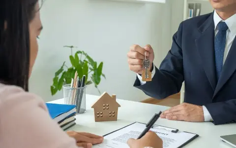 Agente inmobiliario entrega llaves a cliente. Un modelo de casa y un contrato sobre la mesa, ideal para referencia precios alquiler.