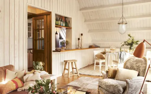 Acogedora buhardilla con encanto, con sofá, sillón estampado, mesa de comedor y cocina abierta.