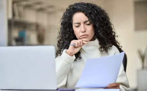 Mujer pensativa revisa documentos, preguntándose si un vecino puede cobrar por llevar la comunidad.