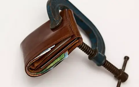 Cartera de cuero apretada en una prensa. El heredero no paga gastos de vivienda, el dinero está bajo presión.