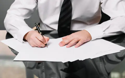 Hombre con camisa blanca y corbata negra escribe en una hoja de aprecio.