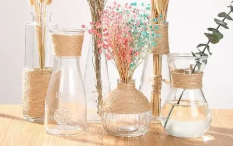 Botellas de cristal decoradas con cuerda, con flores secas y una rama de eucalipto.