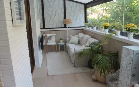 Acogedor salón en terrazas cerradas con encanto, con sofá, silla, plantas y vistas al exterior.