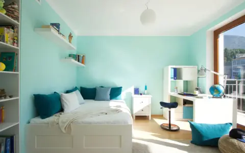 Habitación con pared verde menta y gris, cama blanca, estanterías y escritorio.