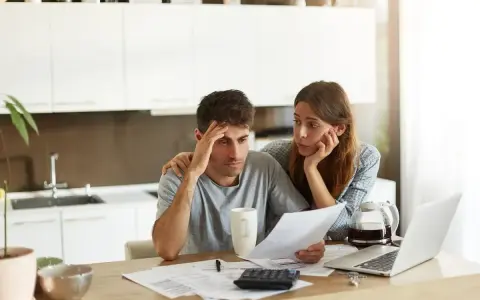 Pareja preocupada revisando facturas. Ella le pone una mano en el hombro, pensando en cómo poner propiedad a nombre de otra persona.