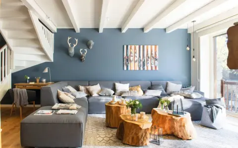 Sofá modular gris y pared azul crean un ambiente acogedor. Mesas de tronco y detalles en madera aportan calidez.