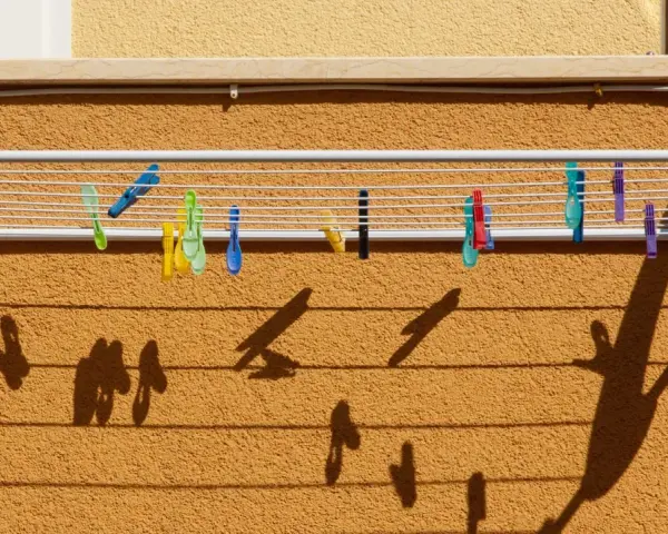 Tendedero exterior con pinzas de colores. Ideas para secar la ropa al sol, creando sombras divertidas en la pared.