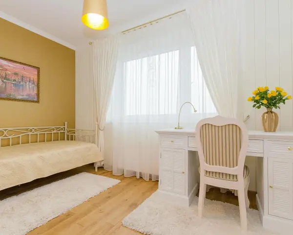 Dormitorio con paredes doradas, cama blanca y escritorio. Los colores que combinan con el amarillo en paredes son el blanco y los tonos tierra, creando un ambiente cálido y luminoso.