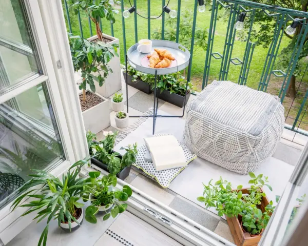Acogedor rincón en unas terrazas cerradas pequeñas, con plantas, cojines, un libro y un café con cruasanes.