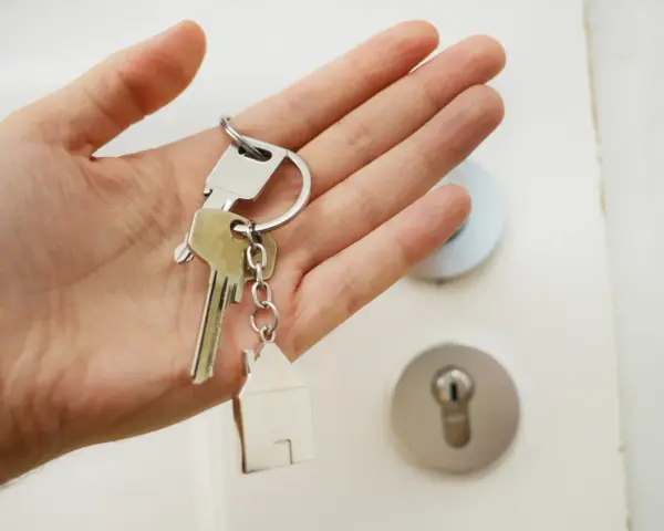 Mano sosteniendo llaves con un llavero de casa. ¡Por fin llega el día cuando pagan la ayuda del alquiler y se puede empezar a soñar con un nuevo hogar!