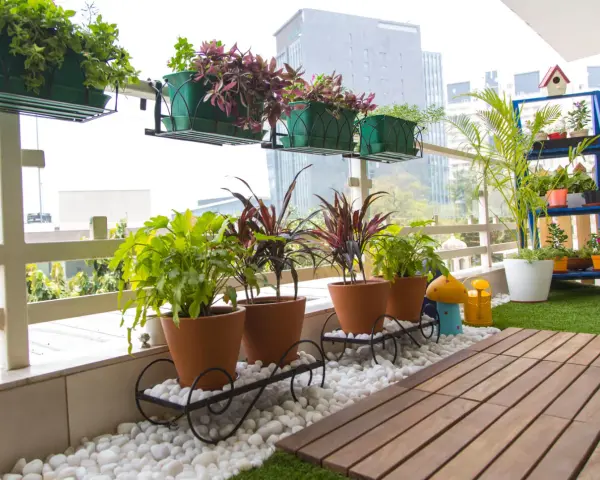 Balcón lleno de plantas en macetas, ideal para decorar terrazas barato. Césped artificial y suelo de madera completan el espacio.
