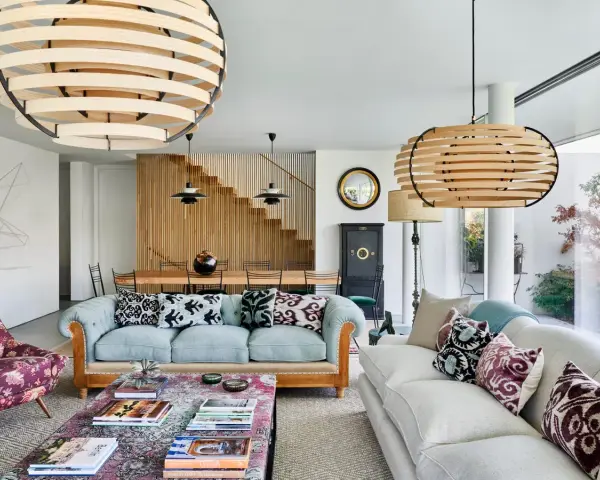 Elegante salón con sofás claros, mesa de centro con libros y lámparas de madera. El minimalismo en casa se refleja en la escalera de madera y la decoración cuidada.