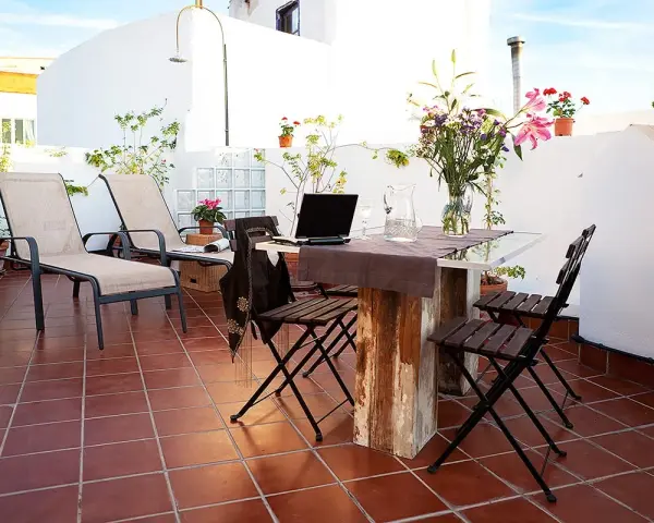 Terraza con tumbonas, mesa y sillas, ideal para uso privativo. Flores y plantas decoran el espacio.