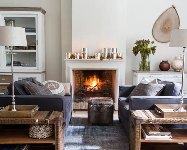 Ideas para decorar la repisa de una chimenea: velas, piñas y un jarrón con ramas secas crean un ambiente acogedor.