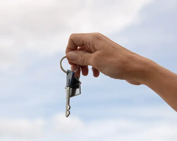 Mano sostiene un llavero con dos llaves y un dije de casa. La custodia llaves comunidad representa el acceso a un hogar compartido.