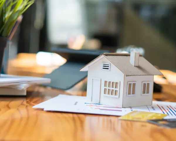 Maqueta de casa sobre gráficos, sugiriendo cómo saber si una casa tiene cargas. Llaves y tarjetas de crédito cerca.