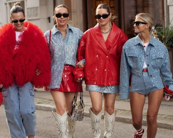 Cuatro mujeres pasean con atuendos llamativos. Una lleva un abrigo rojo voluminoso, otra un conjunto de lentejuelas azules y falda roja. Los colores que pegan con el rojo son el azul y el plateado.