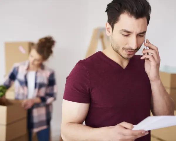 Hombre habla por teléfono, revisando papeles, mientras una mujer desempaca. Quizás buscando como saber a quien pertenece un terreno.