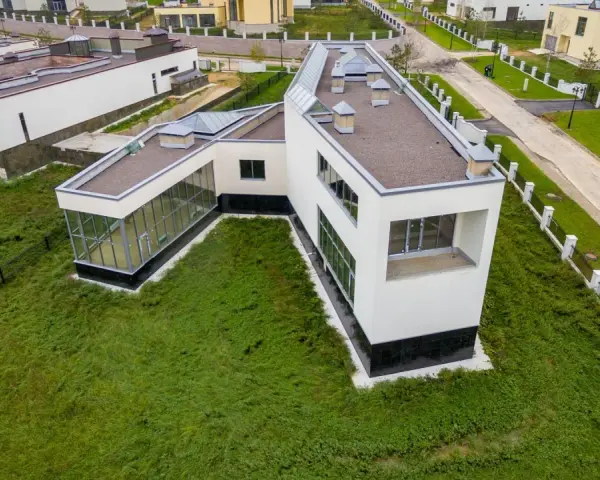 Casa moderna con grandes ventanales y tejado plano, rodeada de césped. Se puede poner una casa prefabricada en un terreno urbano como esta.