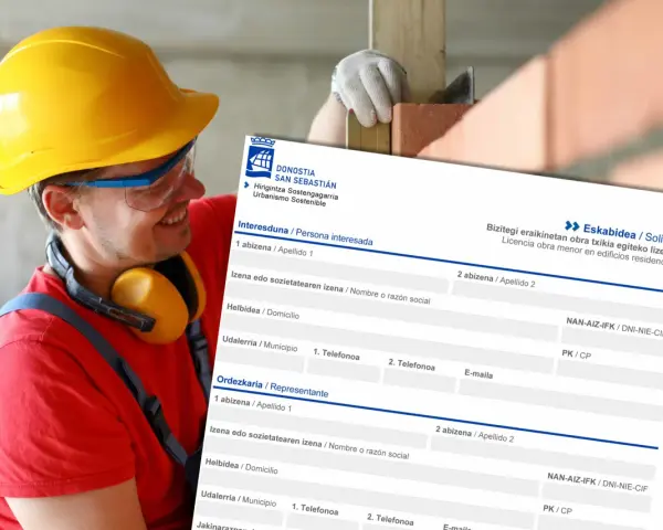 Obrero con casco amarillo sonríe mientras revisa un formulario de solicitud de licencia de obra menor en edificios residenciales.
