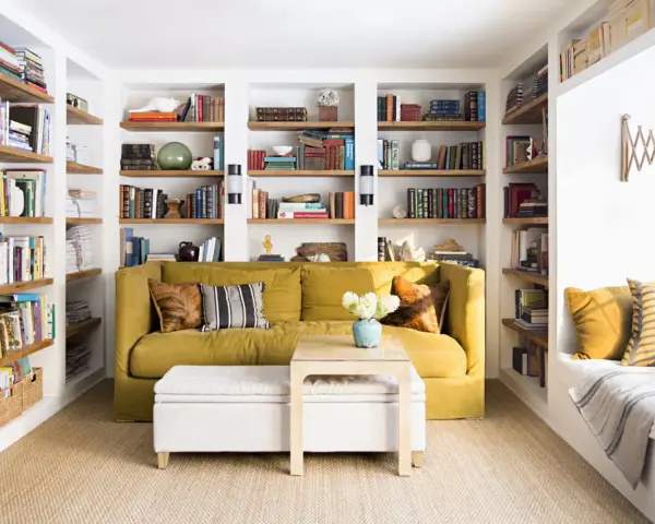 Sofá amarillo y estanterías llenas de libros, como si fueran casas que no necesitan permiso de obra. Un espacio acogedor para leer.
