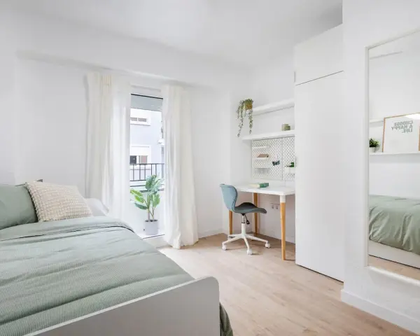 Habitación de estudiante con cama, escritorio, silla y espejo.