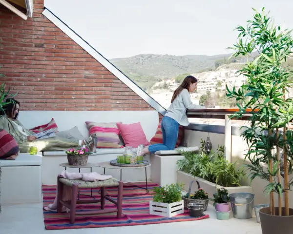 Dos mujeres disfrutan de una terraza con arboles bonitos, cojines coloridos y vistas a la montaña.