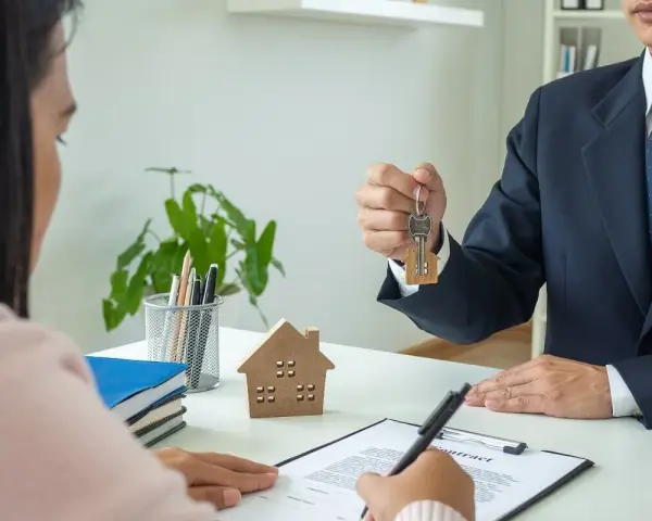 Agente inmobiliario entrega llaves a cliente. Un modelo de casa y un contrato sobre la mesa, ideal para referencia precios alquiler.