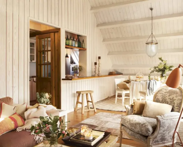 Acogedora buhardilla con encanto, con sofá, sillón estampado, mesa de comedor y cocina abierta.