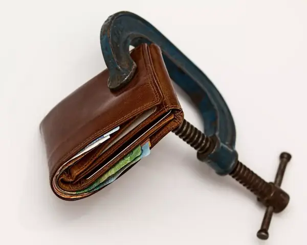 Cartera de cuero apretada en una prensa. El heredero no paga gastos de vivienda, el dinero está bajo presión.