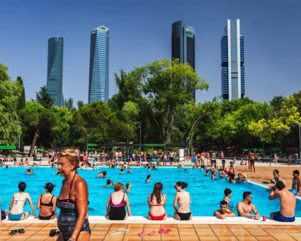 Gente disfrutando en una vibrante piscina comunitaria, con rascacielos modernos de fondo y árboles frondosos.